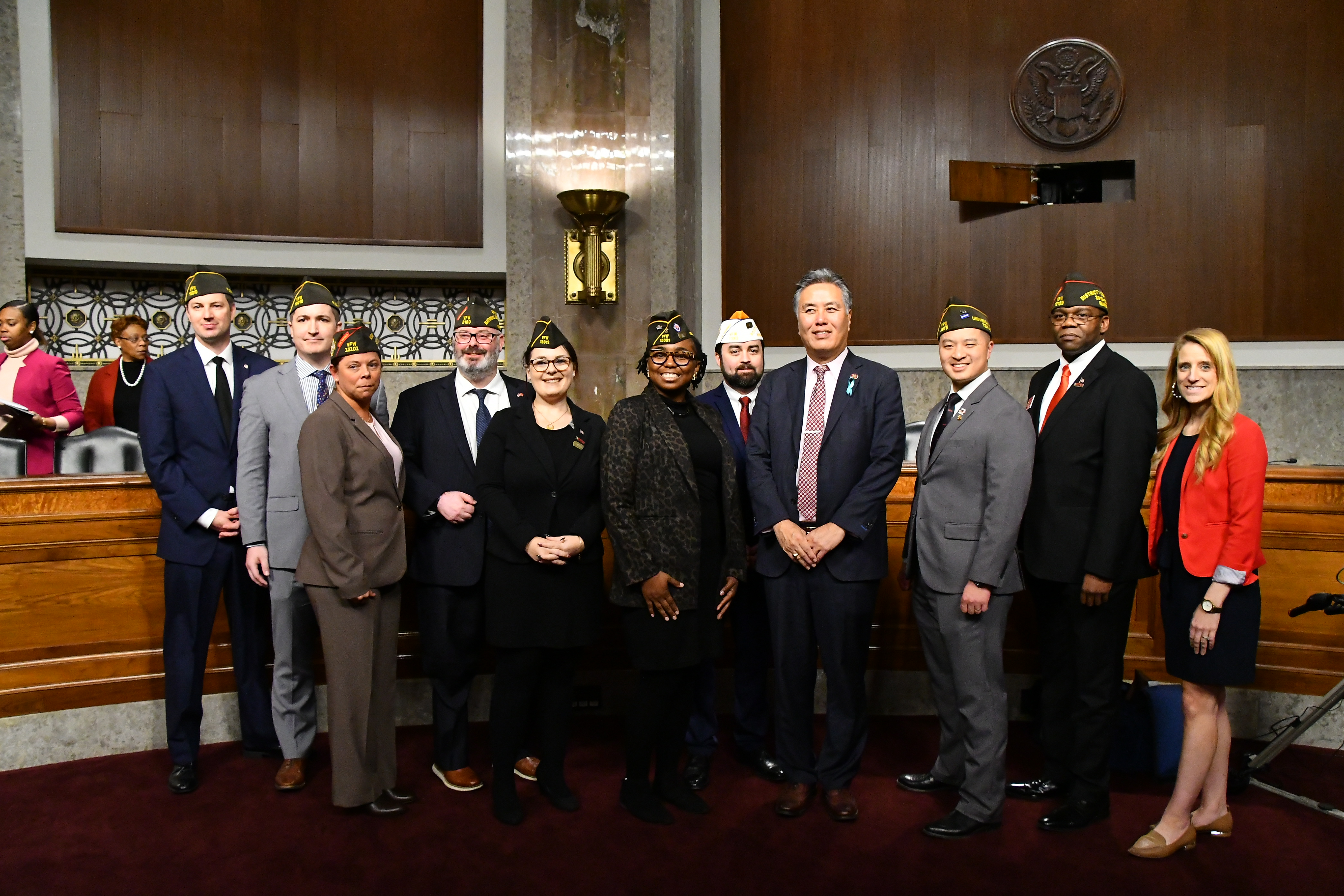 VFW delegation of veterans in garrison caps standing with a member of Congress in a U.S. Senate hearing room.