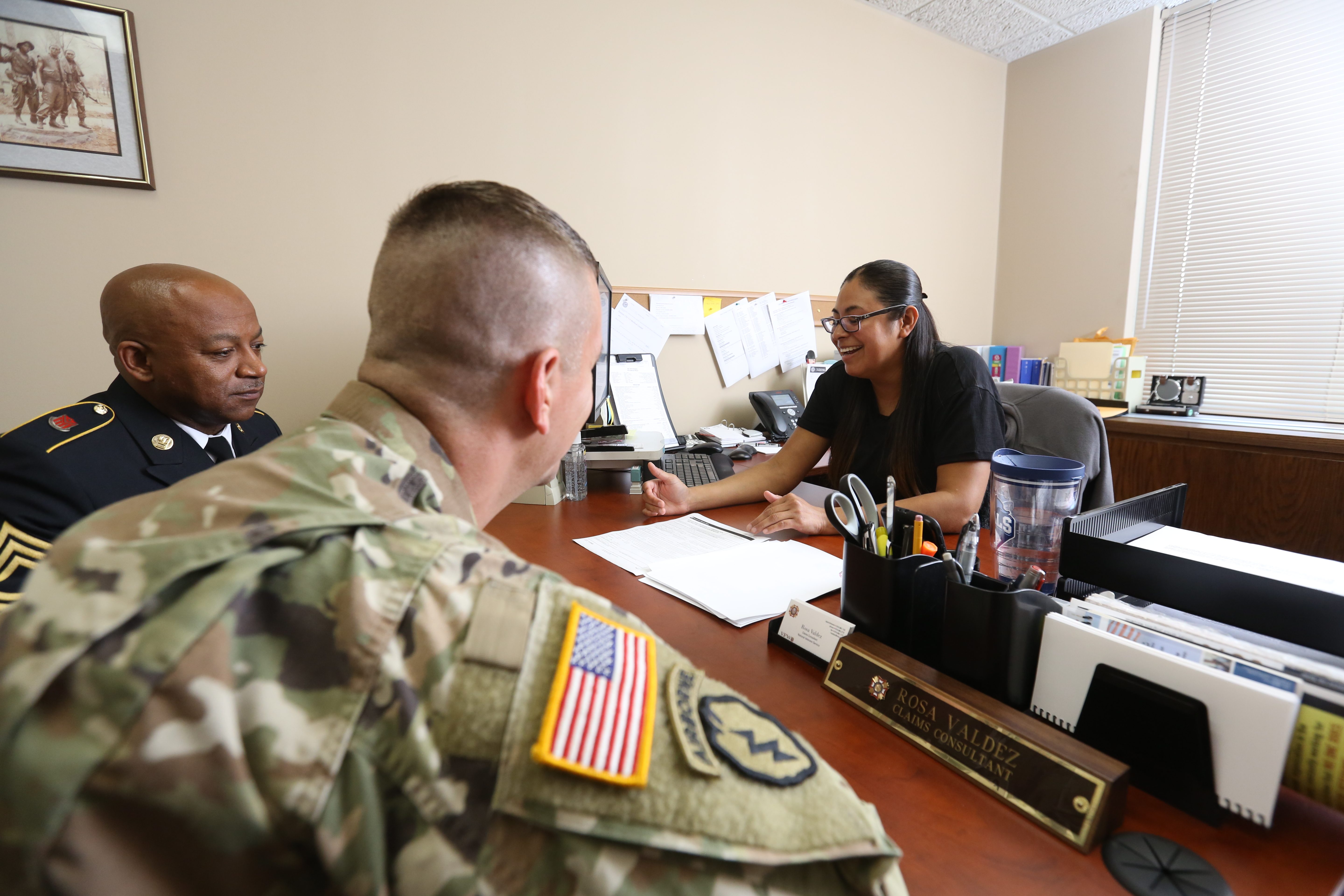 VFW claims consultant meeting with two service members at her desk to review benefits paperwork.